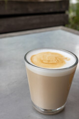 latte with foam in transparent glass on wooden table in cafeteria. There are plants indoors. Cozy atmosphere in cafe for breakfast 