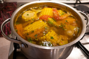close up view of delicious chicken soup with vegetables, corn and herbs. Soup is boiling in the pot on the kitchen oven, cooking process 