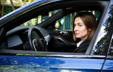 Portrait of young attractive business woman in black suit driving in her luxury car. Business transportation concept