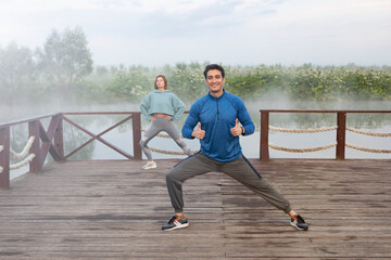 Young sporty couple training on wooden platform on the foggy river at the morning time. Healthy lifestyle concept 