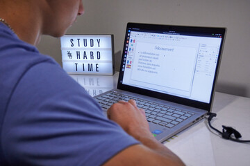 A closeup of an unrecognizable student using the laptop with text study hard time on a table in the...