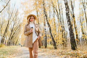 Pretty young woman with coffee cup in the autumn park