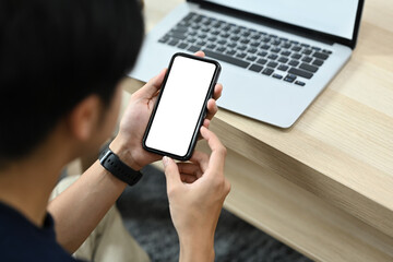 View over shoulder asian man sitting in living room and using mobile phone.
