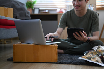 Young business man answering customers through laptops and preparing parcel boxes of product for delivery