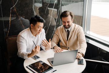Adult multiracial businessmen using laptop while sitting by table
