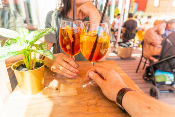 Woman and man making a celebratory toast with aperol spritz orange alcoholic cocktails at outdoors cocktail bar.Close up.