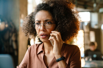 Young african american woman using cellphone while working in cafe