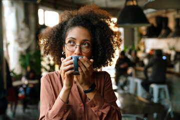 Young african woman wearing eyeglasses drinking coffee in cafe