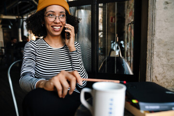 Young african woman smiling while talking on cellphone in cafe