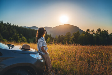 Woman traveler looking at the sunset in the field in the mountains standing near car - 522429370