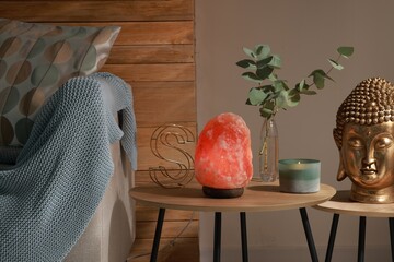 Beautiful Himalayan salt lamp, golden Buddha sculpture and decor on wooden tables in living room