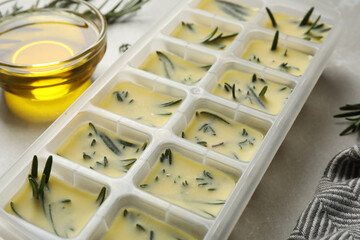 Ice cube tray with herbs frozen in oil and fresh rosemary on grey table, closeup