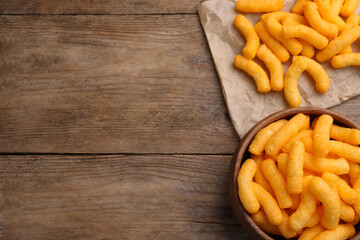 Many tasty cheesy corn puffs on wooden table, flat lay. Space for text