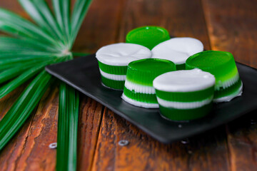 Pandan coconut milk jelly served in a black plate on a wooden table with banana leaves beside.