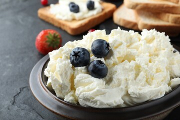 Tasty cream cheese and fresh berries on black table, closeup