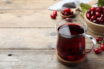 Glass cup of fresh dogwood tea with berries on wooden table. Space for text