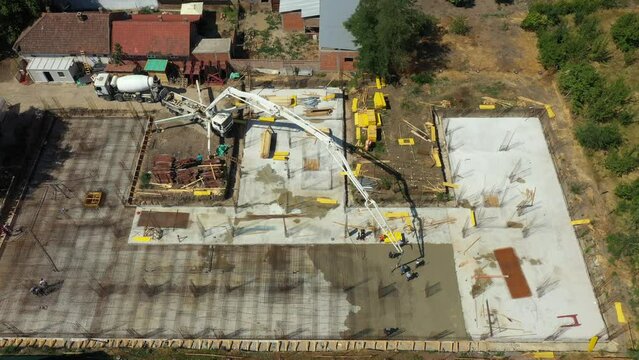 Aerial view construction site, mixer truck pouring concrete into pump machine pumping to exit tube, worker is directing the on right direction, building foundation. Riggers, workers leveling concrete
