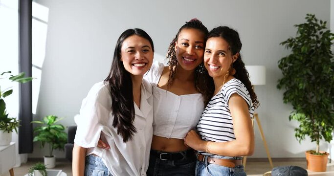 Multi ethnic girlfiends standing with arms aroung in modern home