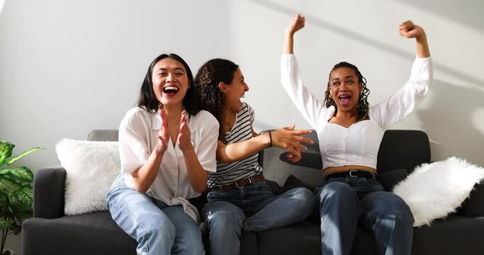 Excited girlfriends sitting on couch cheering while watching TV