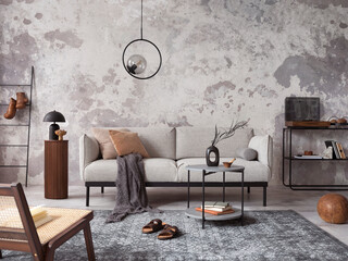 Exquisite and modern composition of living room interior with design grey sofa, furnitures, round pedant lamp, black coffee table, decoration, pillow and elegant accessories. Concrete grunge wall.