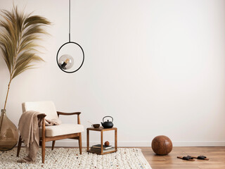 Interior design of aesthetic and minimalist living room with boucle armchair, wooden coffee table, pedant lamp, beautiful leafs in vase, decoration and personal accessories. Copy space. Home decor.