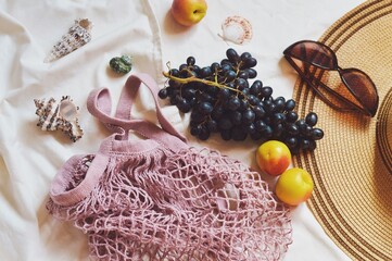 Summer beach picnic aesthetics. Fishnet bag, black grapes, nectarines, seashells, hat and sunglasses. Travel flat lay photo