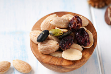 Various of berry, nuts and seeds in a wooden bowl on a light wooden table.