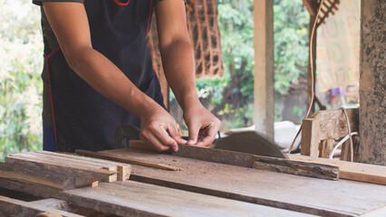 Asian carpenter is using a circular saw to cut wood to construct a storage box on a desk table at his factory. Working as your own boss at home concept