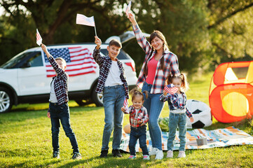 American family spending time together. With USA flags against big suv car outdoor.