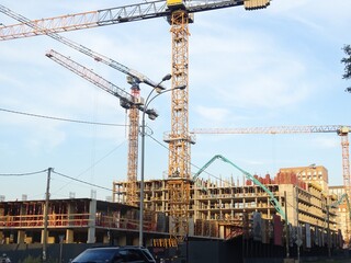 Full-color horizontal photo. A huge construction site. Several tower cranes and other large construction equipment. A grid of supports with fittings and floor coverings.