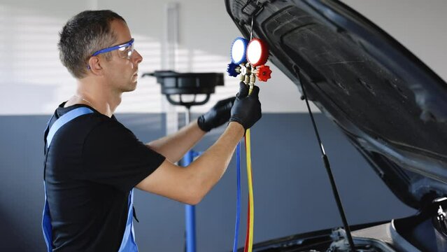 Car mechanic with manometer to fill the gas in the car air conditioning compressor. Service of checking the car air conditioner. Refrigerant recharge system