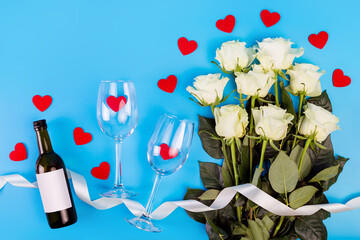 Top view photo of romantic evening, dinner decor hearts love wineglasses with confetti wine bottle and white tape with large bouquet of white roses on isolated blue background with copyspace