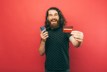 A picture of a man happily holding his credit card and phone making some online shopping