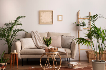 Fototapeta premium Boho and cozy interior of living room with design beige sofa, pillows, mock up poster frames, rattan coffee tables, plants, bamboo ladder, decoration and personal accessories. Home decor. Template.