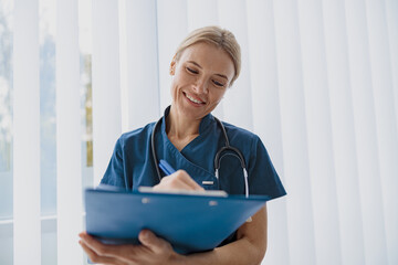 Smiling woman doctor taking notes on clipboard during appointment in medicine center