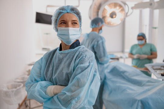 Female surgeon in mask standing in operating room with crossing hands, ready to work on patient