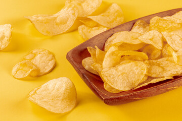 Potato chips or crisps in a bowl and scattered on a yellow background, a close-up