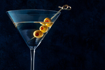 Martini, a glass with spicy olives on a toothpick, on a dark background. Alcoholic cold drink with...