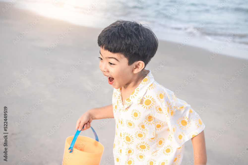 Wall mural cute boy running on the beach. he holds a plastic toy and running happily and happy time.