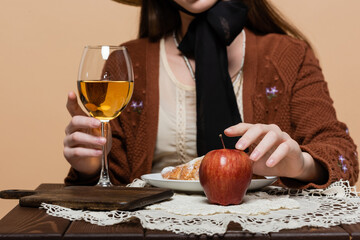 Cropped view of blurred woman touching glass of wine and apple on table isolated on beige