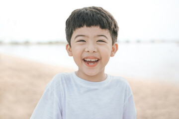 Portrait cute boy playing in the sandy beach, happy and Smiling and fun child. he wears a white shirt.