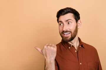 Photo of positive cheerful man look indicate finger empty space blank isolated on beige color background