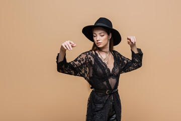 Brunette model in fedora hat and black robe posing isolated on beige