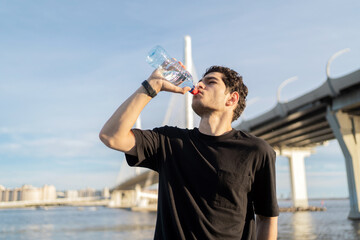 Drinking clean water from a bottle quenches thirst, a male athlete runner does a workout.