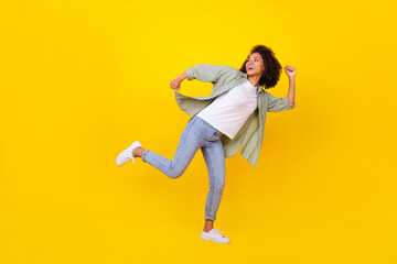 Fototapeta na wymiar Full length photo of charming young girl wavy hair running look empty space dressed stylish khaki shirt isolated on yellow color background
