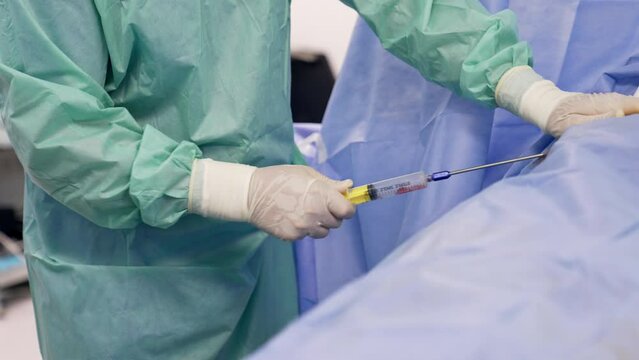 Medic’s hands in gloves shove the syringe into patient’s body. Big syringe is filled with blood of a patient.