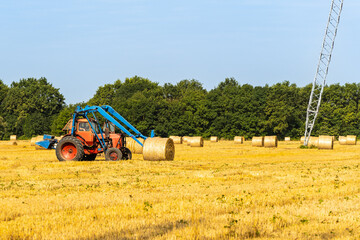 Rolls with straw under VL-750. Straw bales on universal forks mounted on Belarus tractor. Blurred background. Collection of hay bales in place for transportation. Smolenskaya, Russia - July 16, 2022