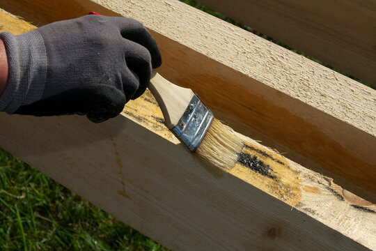 Hand Holds A Brush, Painting And Caring For Wood. Protection Of Wood From Rot. Selective Focus.