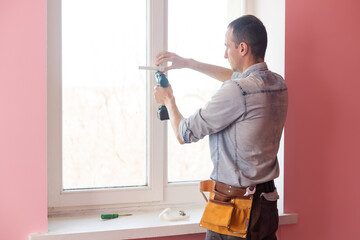 Fototapeta na wymiar Handyman using a cordless screwdriver to install a window handle. Qualified worker services, home repair and renovation.