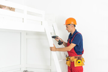 Handyman assembling wooden furniture in children's room.